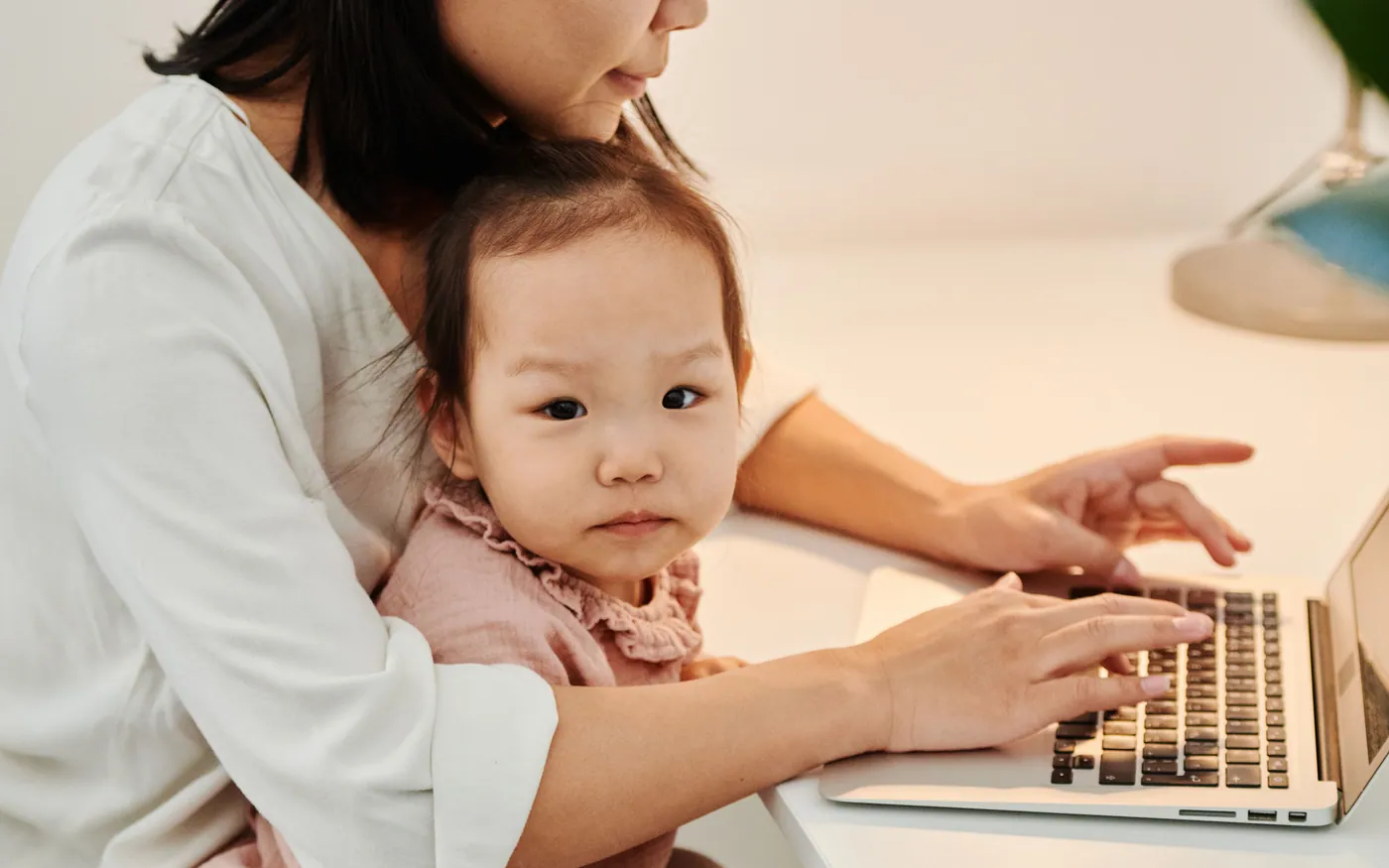 Một người mẹ châu Á làm việc trên máy tính khi ôm con nhỏ