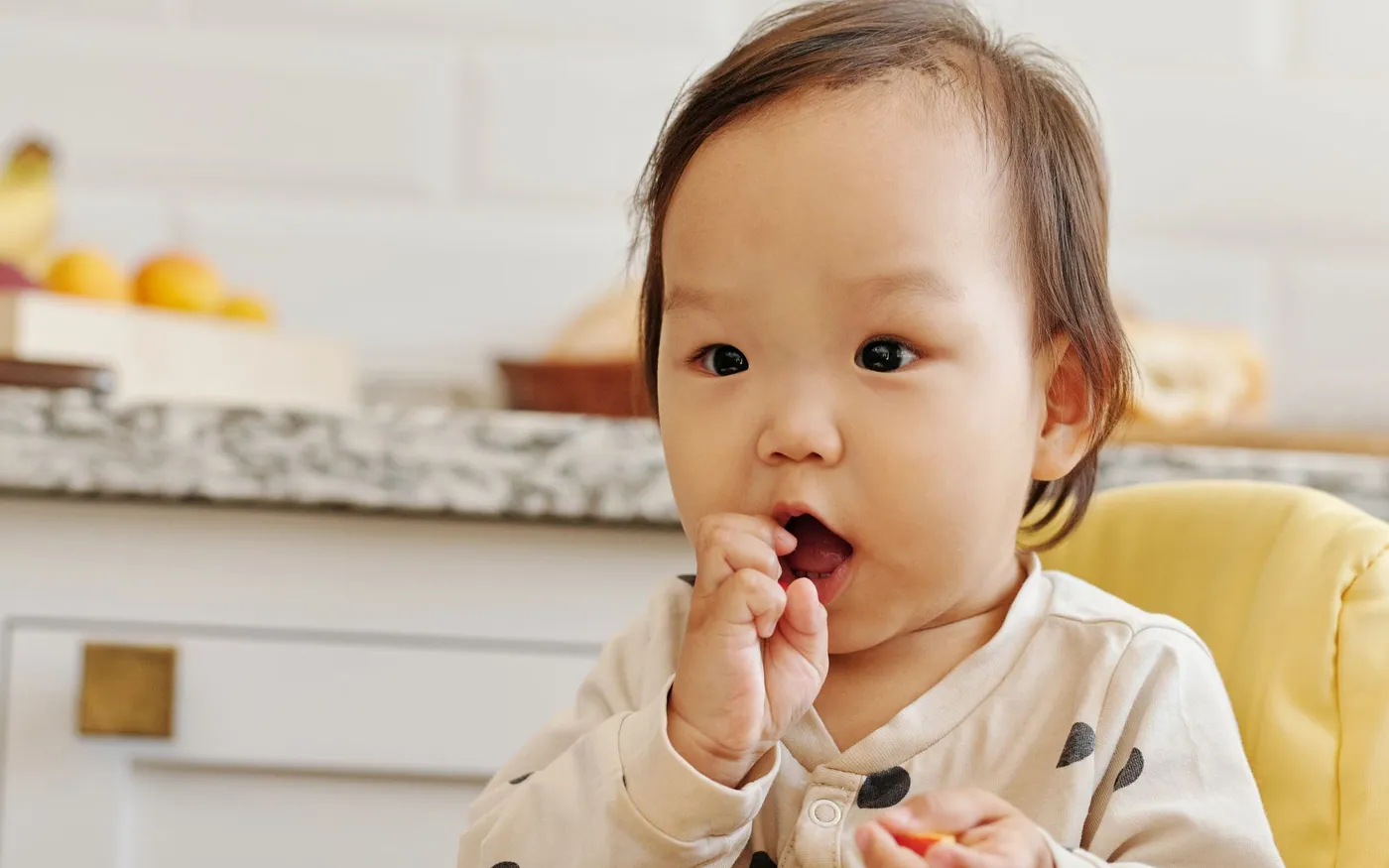 Một em bé châu Á ngồi thẳng trên ghế ăn